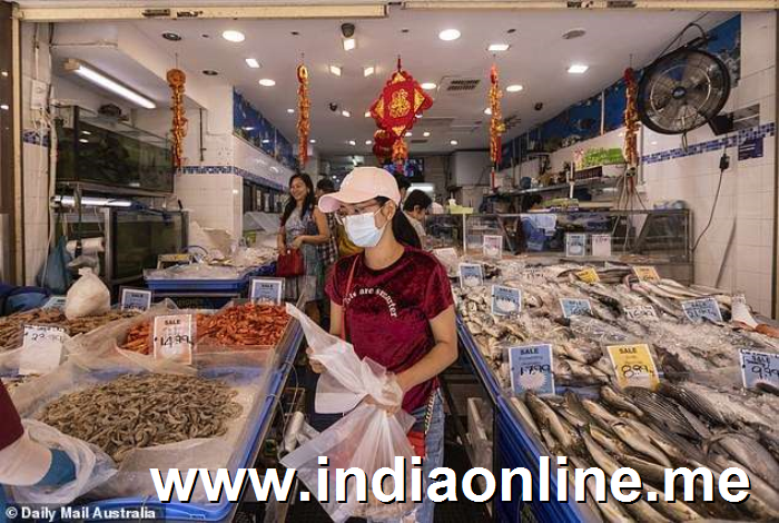 a person preparing food in a kitchen: Shoppers are pictured wearing facemasks at a seafood market in Sydney's Cabramatta (pictured) with the number of people affected in Australia rising to 10