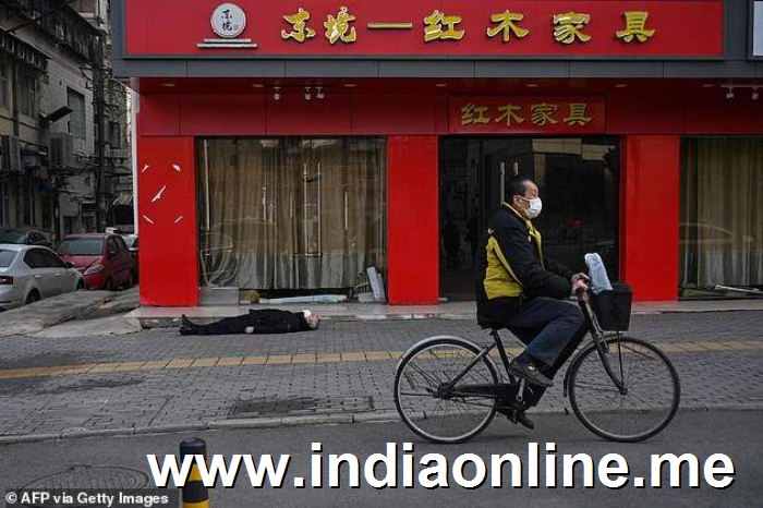 a person riding a bicycle on a city street: A man wearing a face mask cycles past the body of a man who collapsed and died on a pavement in Wuhan (pictured), a city of 1 1million people which is under quarantine